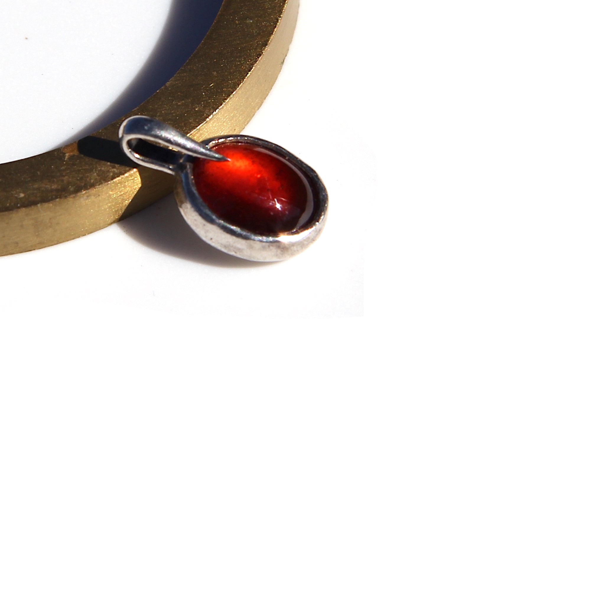 Oval orange Hessonite charm in a silver setting, resting beside a gold-colored circular object